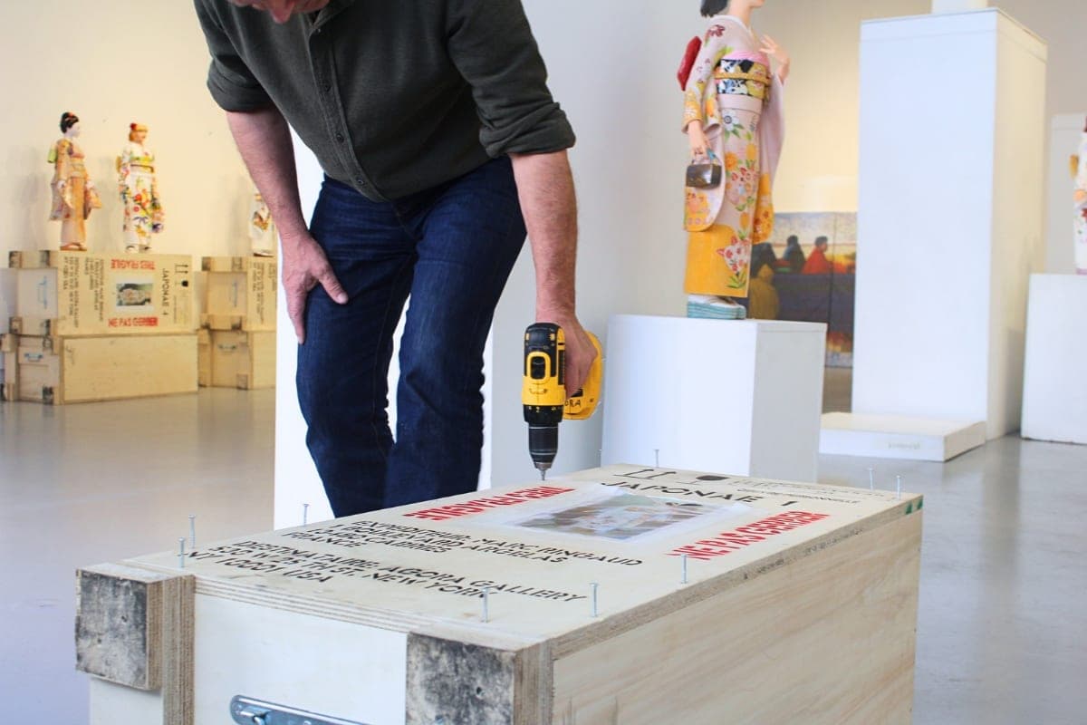 An artist unpacking a wooden shipping crate of his sculptures after delivery to Agora Gallery