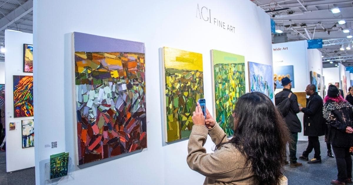 A visitor photographs colorful abstract paintings at AGI Fine Art’s booth at Artexpo New York