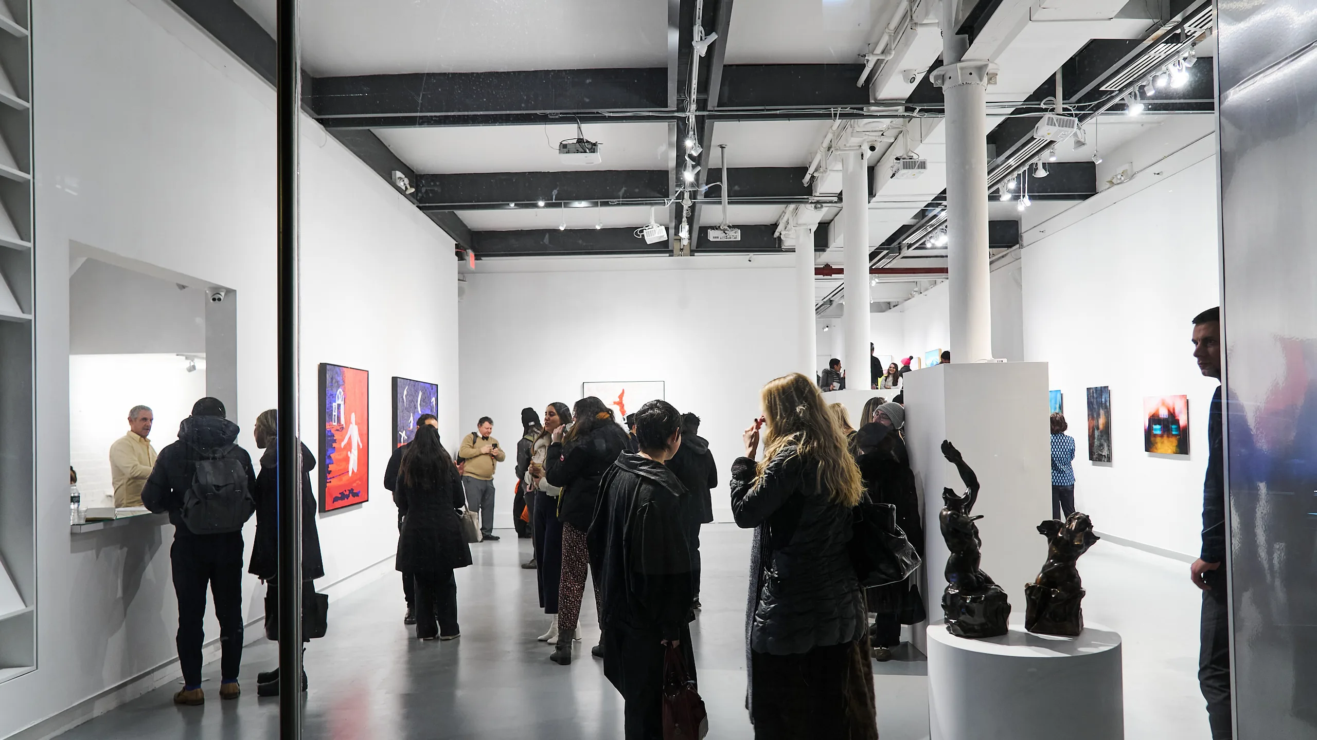 Visitors at a previous A New Gotham exhibition in Agora Gallery's Chelsea space, with paintings on the walls and two bronze sculptures on a plinth