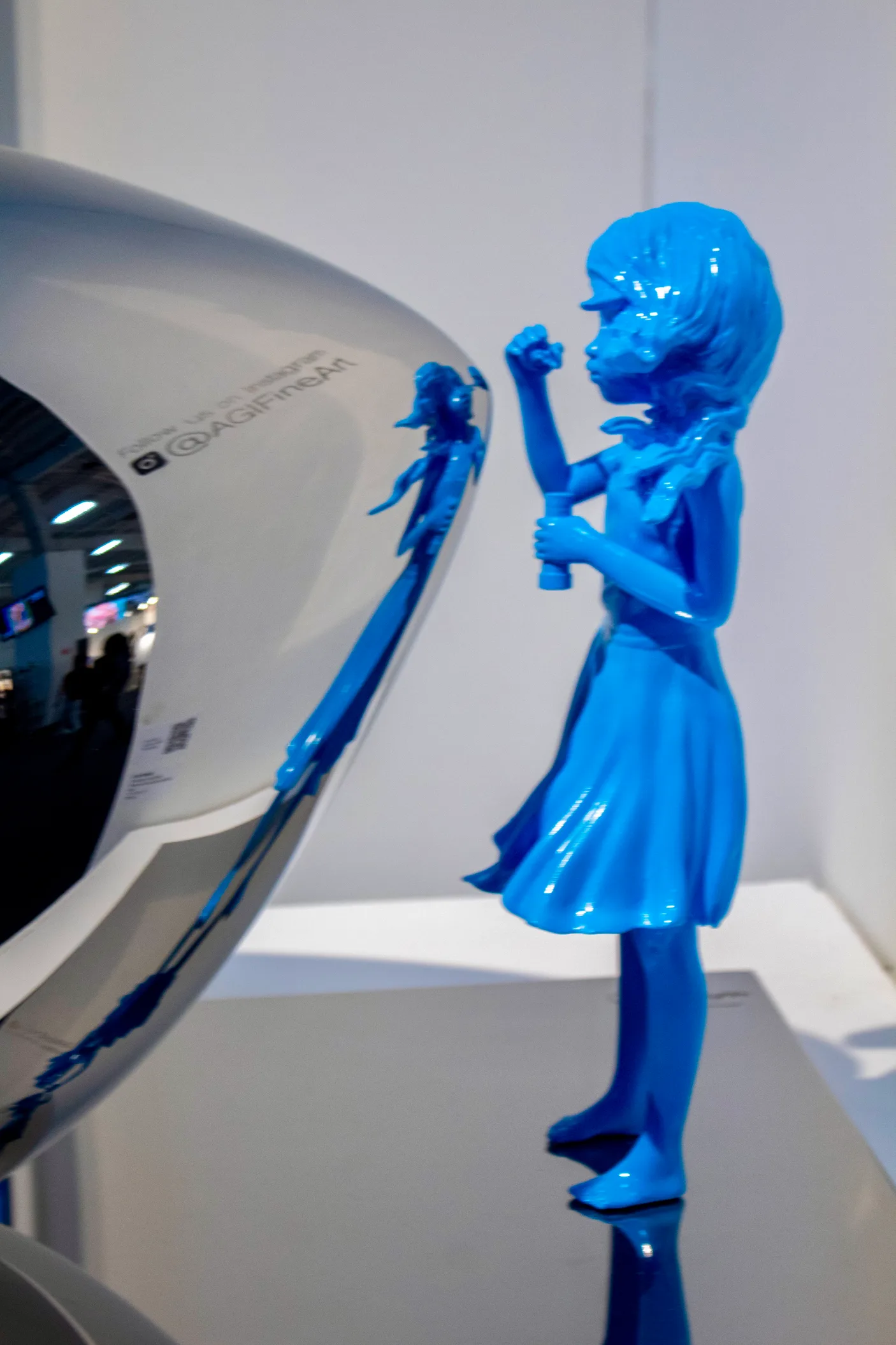 A blue figurative sculpture beside a mirrored form at the AGI Fine Art booth, Artexpo New York