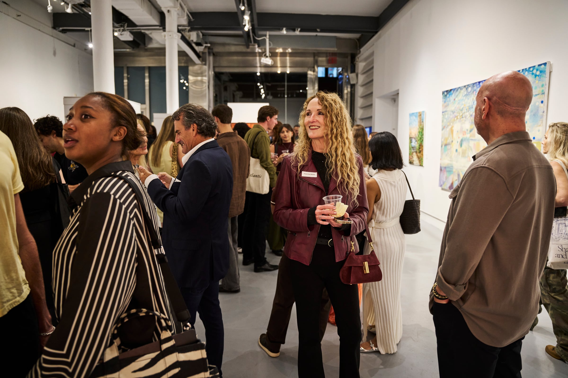 Guests talk and smile in the busy main gallery, drinks in hand