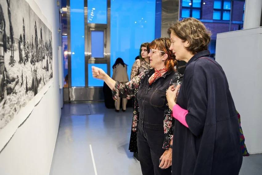 Two visitors talking beside a black and white drawing