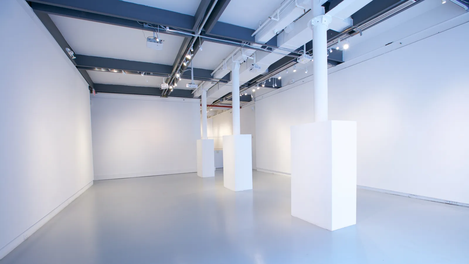 The 530 West 25th Street gallery standing empty, with white display plinths on a grey resin floor under a dark beamed ceiling