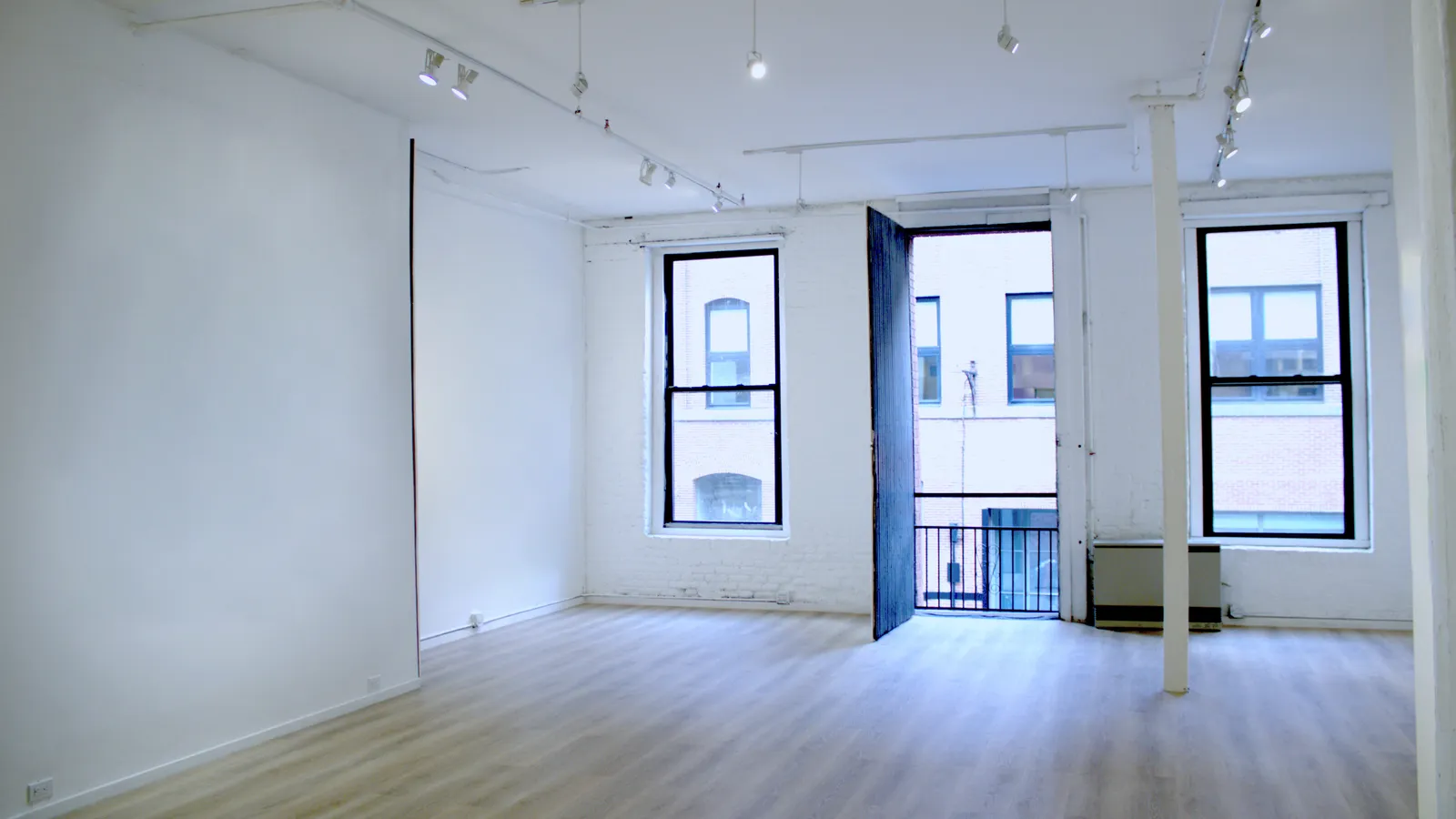 The window wall of The Loft: white-painted exposed brick, two tall sash windows, and a door standing open onto the fire escape