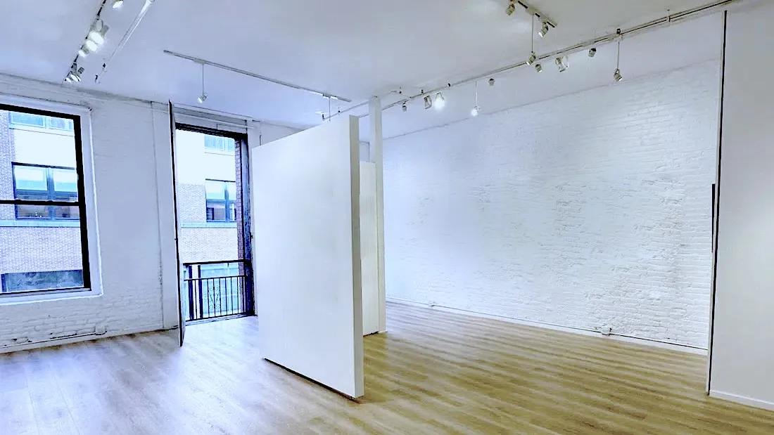 The length of The Loft along its white-painted exposed brick wall, with a movable partition standing on the wood plank floor