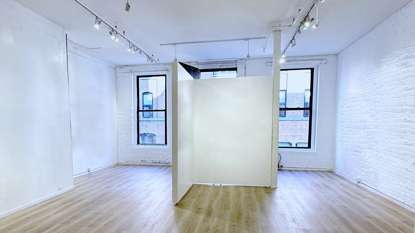 A free-standing partition set up in the middle of The Loft between two tall windows, dividing the wood-floored room