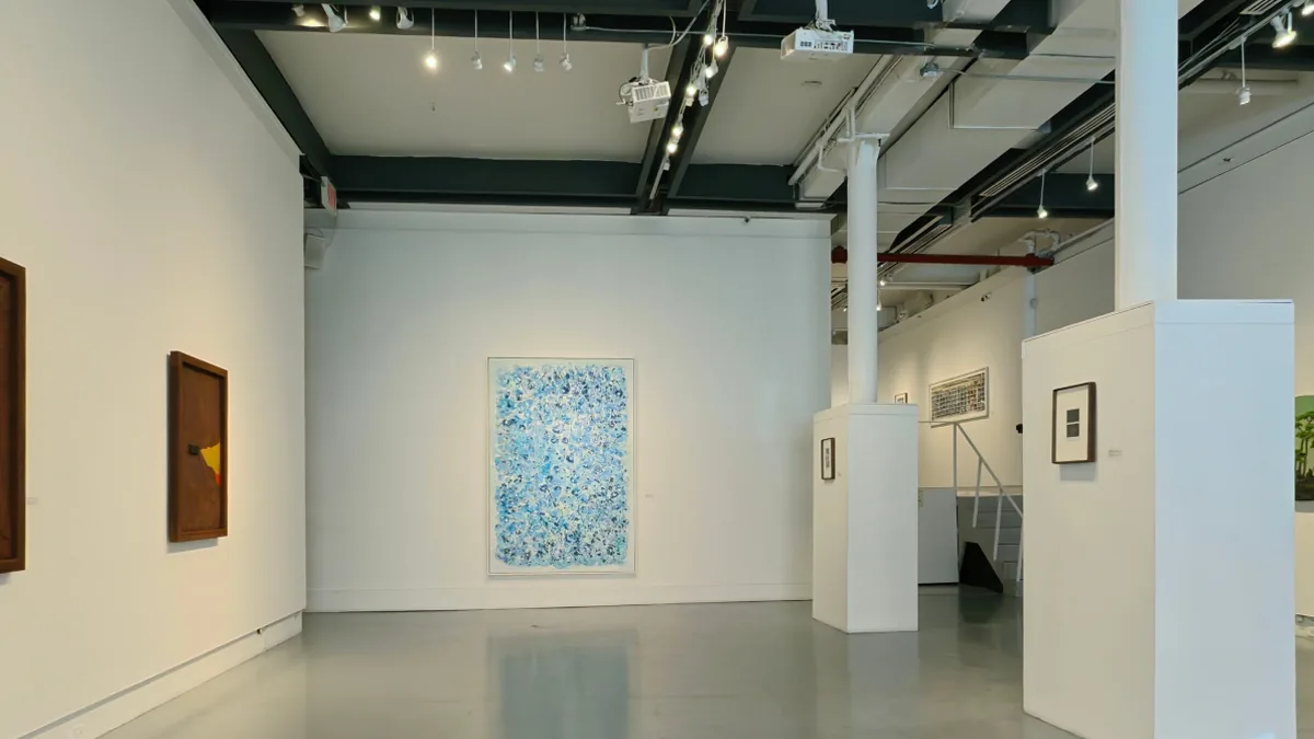The same gallery with an exhibition installed: framed paintings hung along the walls and smaller works on plinths