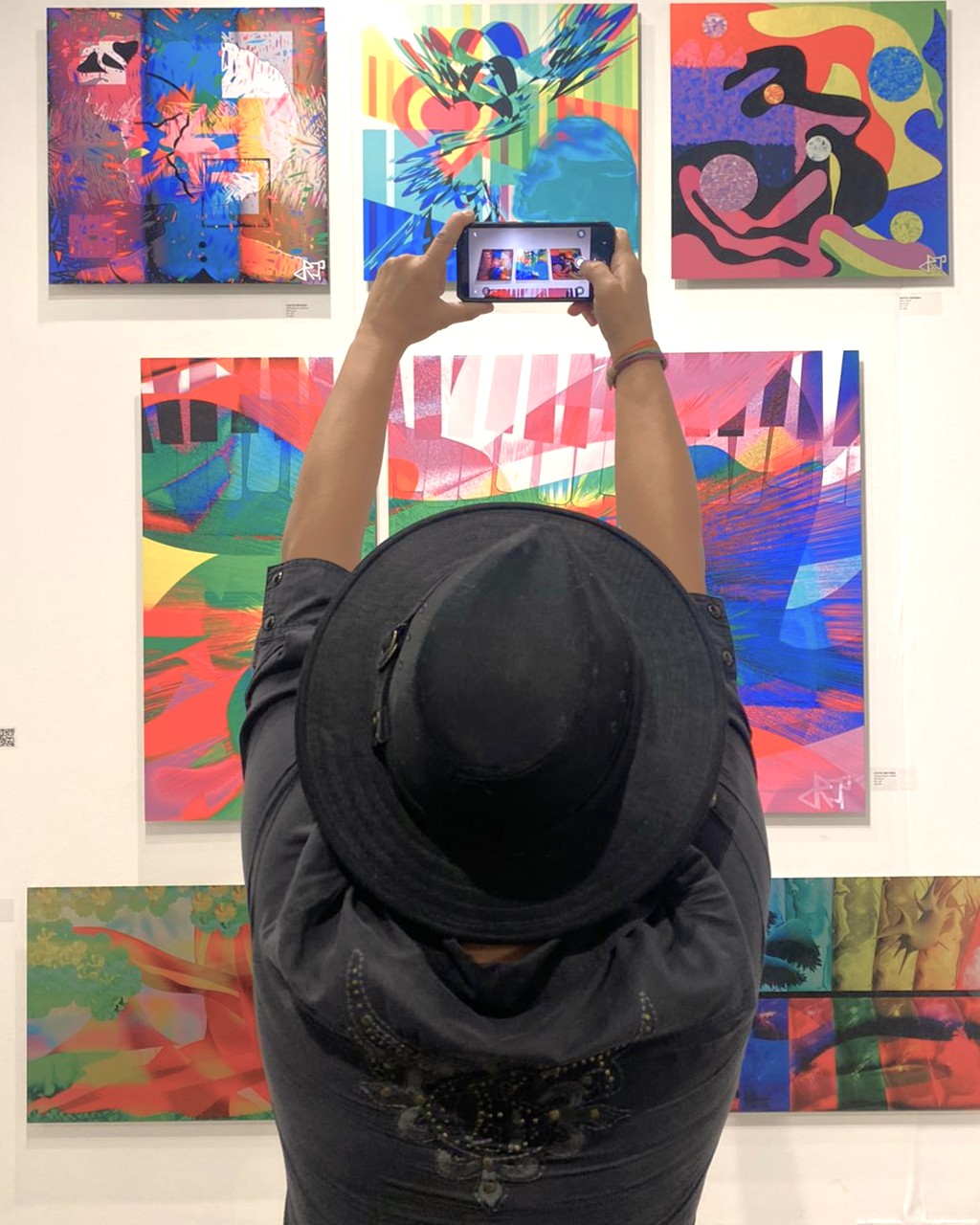A visitor photographing a wall of paintings at the AGI Fine Art booth, Red Dot Miami