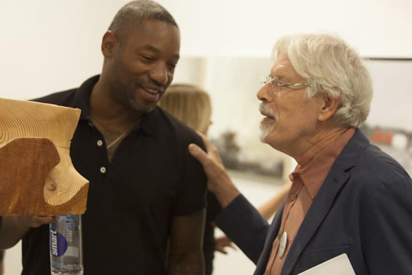 Artist Walter Bruszewski speaking with a guest in front of his wooden sculpture at the opening reception for his exhibition