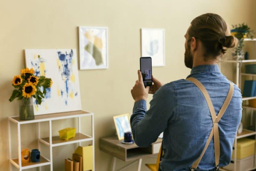 Portrait of man taking photo of painting to upload to Facebook Business Page