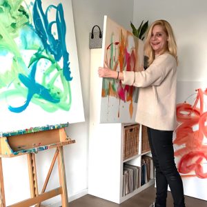 Agora artist Katja van den Bogaert holding one of her abstract paintings in her studio.