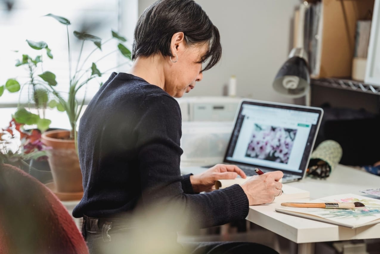 Artist working at a computer with artwork displayed on screen in her studio.