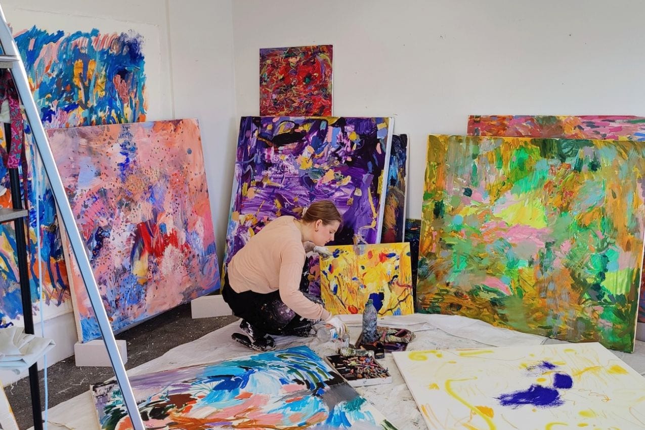 Artist Sanna Vakkilainen working among paintings in her studio.