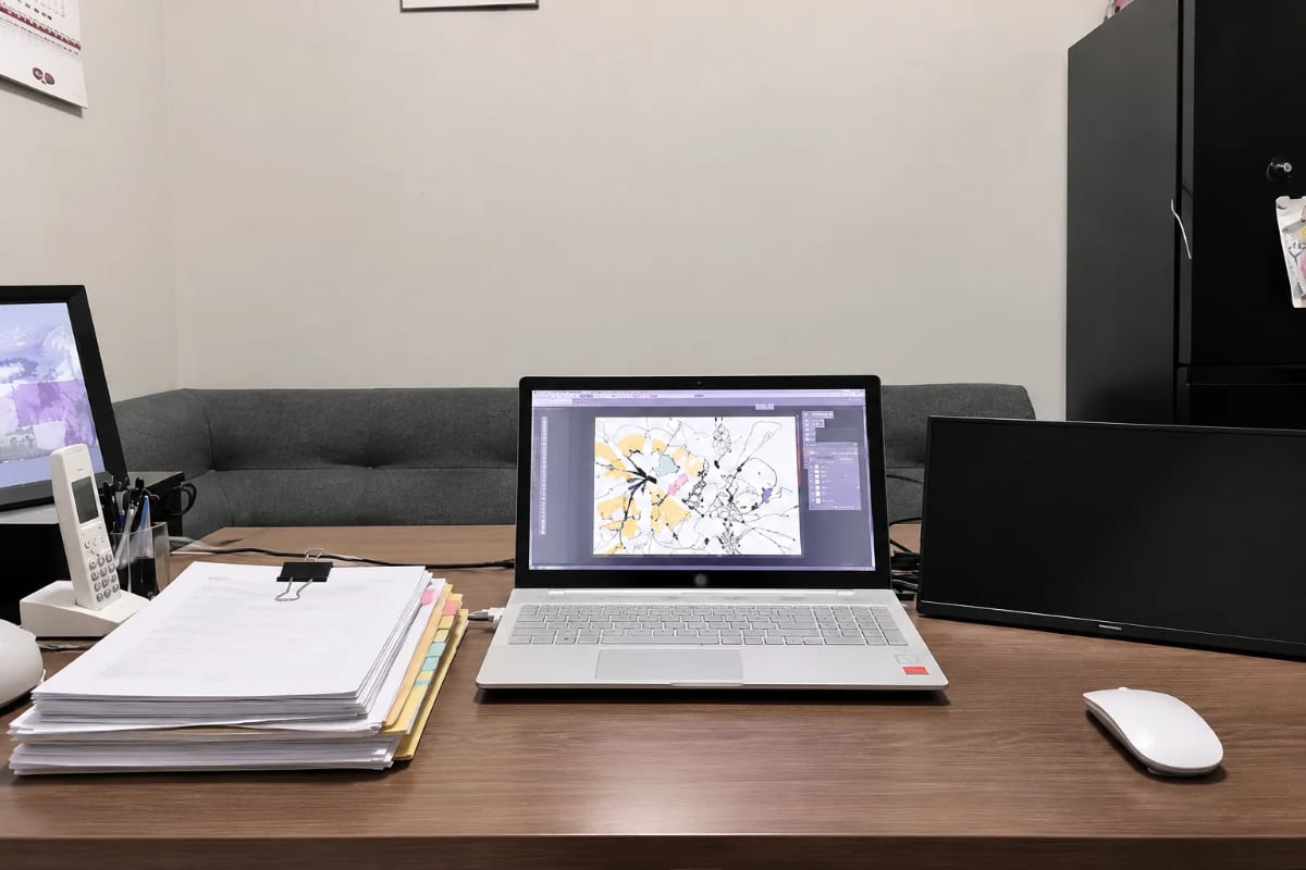 Artist’s desk with a laptop showing an illustration beside a tabbed stack of tax records ready for the accountant