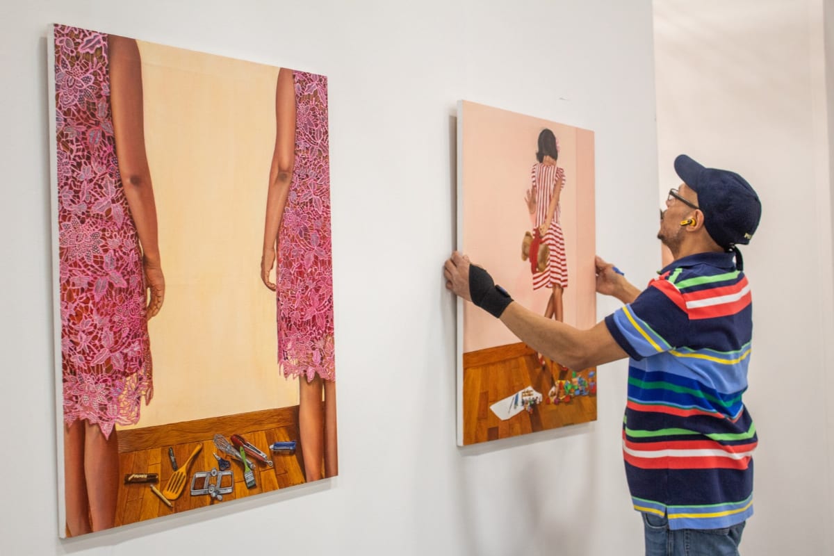 A man levels a large figurative painting by artist Shubhi Gupta while installing work at Artexpo New York.