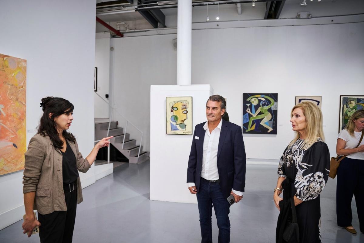 AGI Fine Art’s Director discusses the exhibition with two exhibiting artists at Agora Gallery in Chelsea, with paintings displayed throughout the gallery.